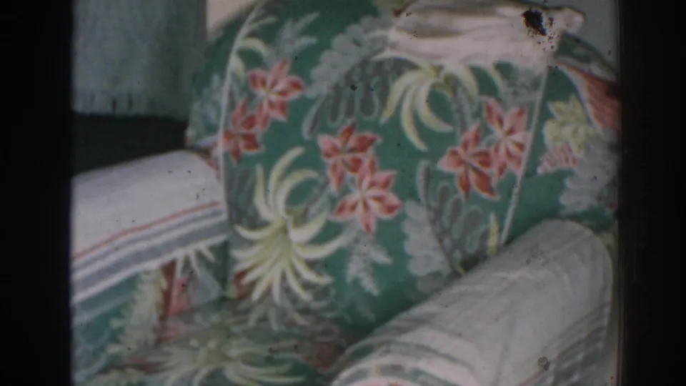 1963 New Jersey 8mm frame centered on a tropical floral armchair with cream arm covers and visible film-edge wear.
