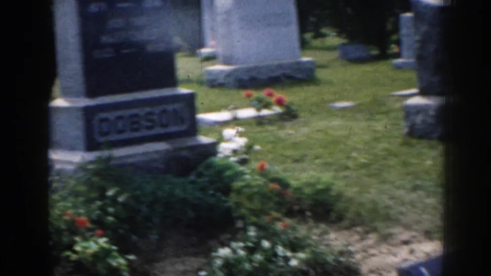 1963 New Jersey 8mm frame showing an upright Dobson gravestone, surrounding lawn, flowers, and other markers.