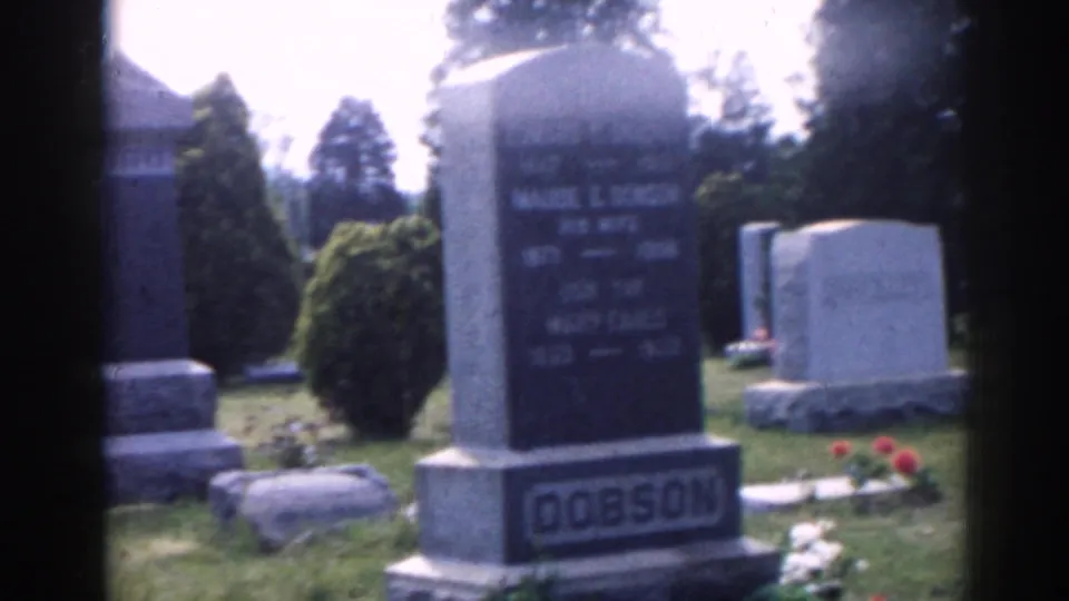 1963 New Jersey cemetery view with a prominent upright monument, surrounding headstones, lawn, shrubs, and bright daylight.