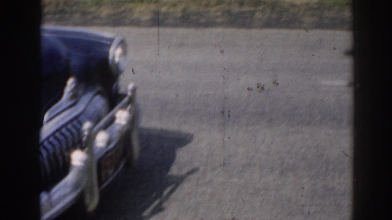 Close 8mm view of the front of a dark blue vintage sedan in New Jersey, with rounded fenders, chrome grille, and headlights visible.
