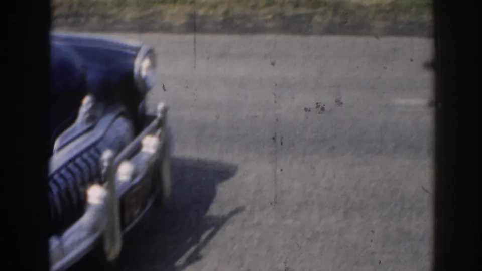 Close 8mm view of the front of a dark blue vintage sedan in New Jersey, with rounded fenders, chrome grille, and headlights visible.