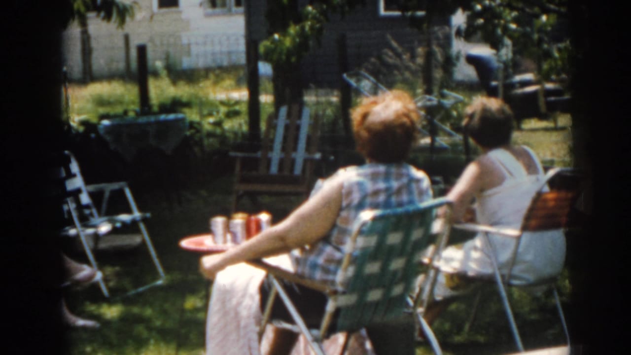 Two women sit beside a small table with drink cans in a backyard.