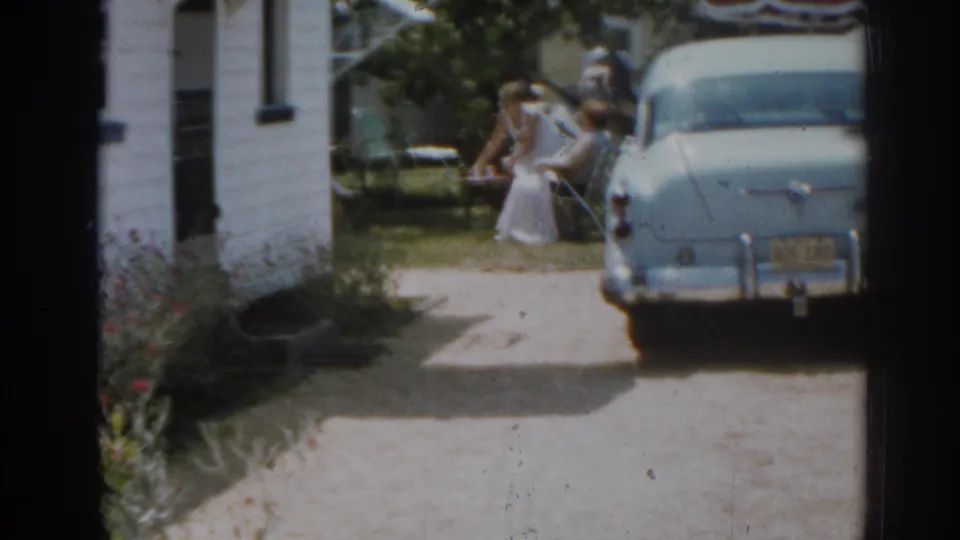 1963 New Jersey backyard view with a blue early-1960s car, white clapboard house, and women near folding lawn furniture.