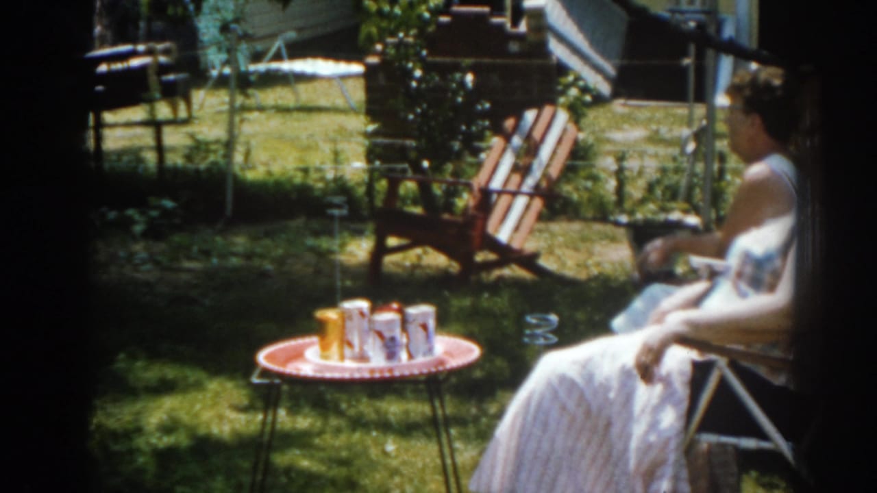 Woman in a lawn chair beside a small table with drinks in a sunny yard.