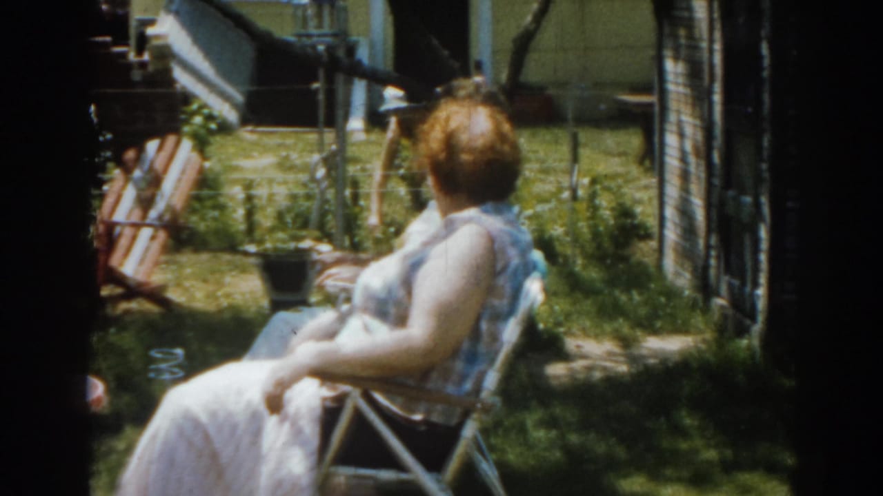 Woman seated outdoors in a lawn chair, seen from behind in a grassy backyard.