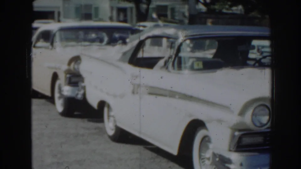 1963 New Jersey home-movie frame showing a white chrome-trimmed sedan with whitewall tires parked ahead of other cars on a residential street.