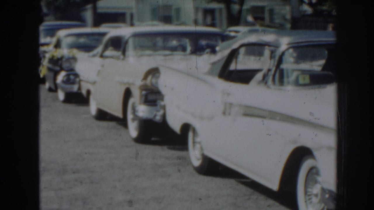 A row of mid-century cars sits along a New Jersey residential street in a soft 8mm frame from the supplied 1963 home movie.
