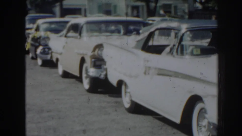 A row of mid-century cars sits along a New Jersey residential street in a soft 8mm frame from the supplied 1963 home movie.
