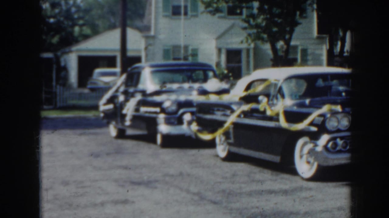 Decorated classic cars parked on a suburban street in front of houses.