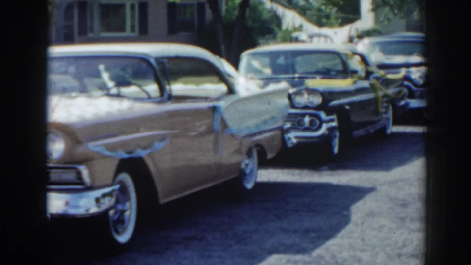 1963 New Jersey frame with a light-colored sedan in the foreground and ribbon-decorated dark cars parked behind it.