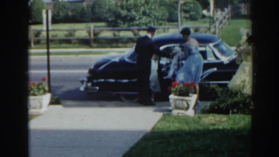 1963 New Jersey home-movie frame showing a woman getting into a black sedan as a man holds position near the open door.