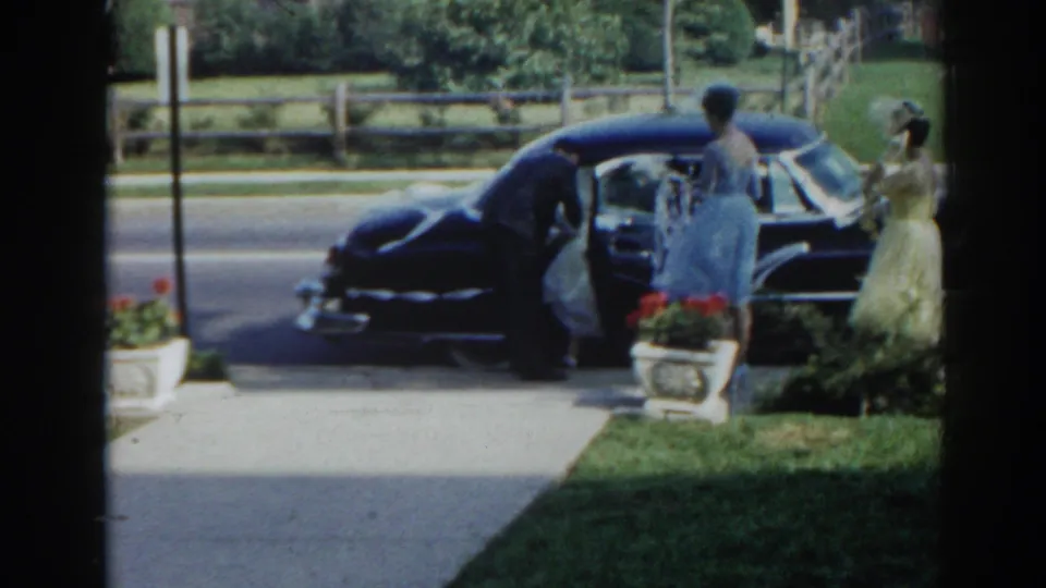 1963 New Jersey frame with a suited man leaning into a black sedan while two women in formal dresses wait nearby.