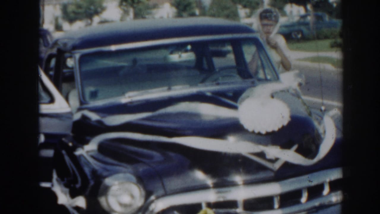 Ribbon-decorated black sedan seen from the front with people standing near it.