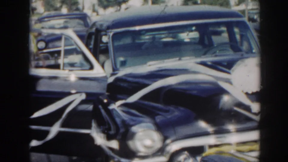 Ribboned black wedding sedan on a New Jersey suburban street, filmed in soft 8mm color during a 1963 wedding departure moment.