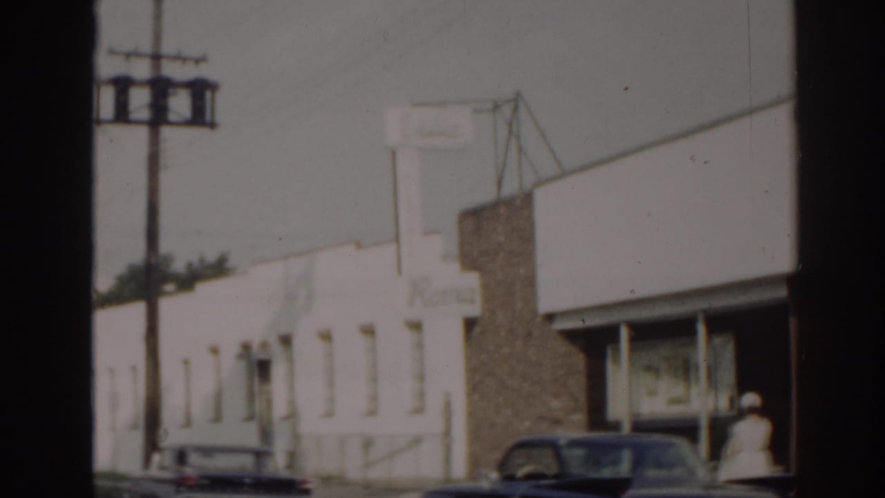 Storefront exterior with parked cars and a person near the right edge by the entrance.