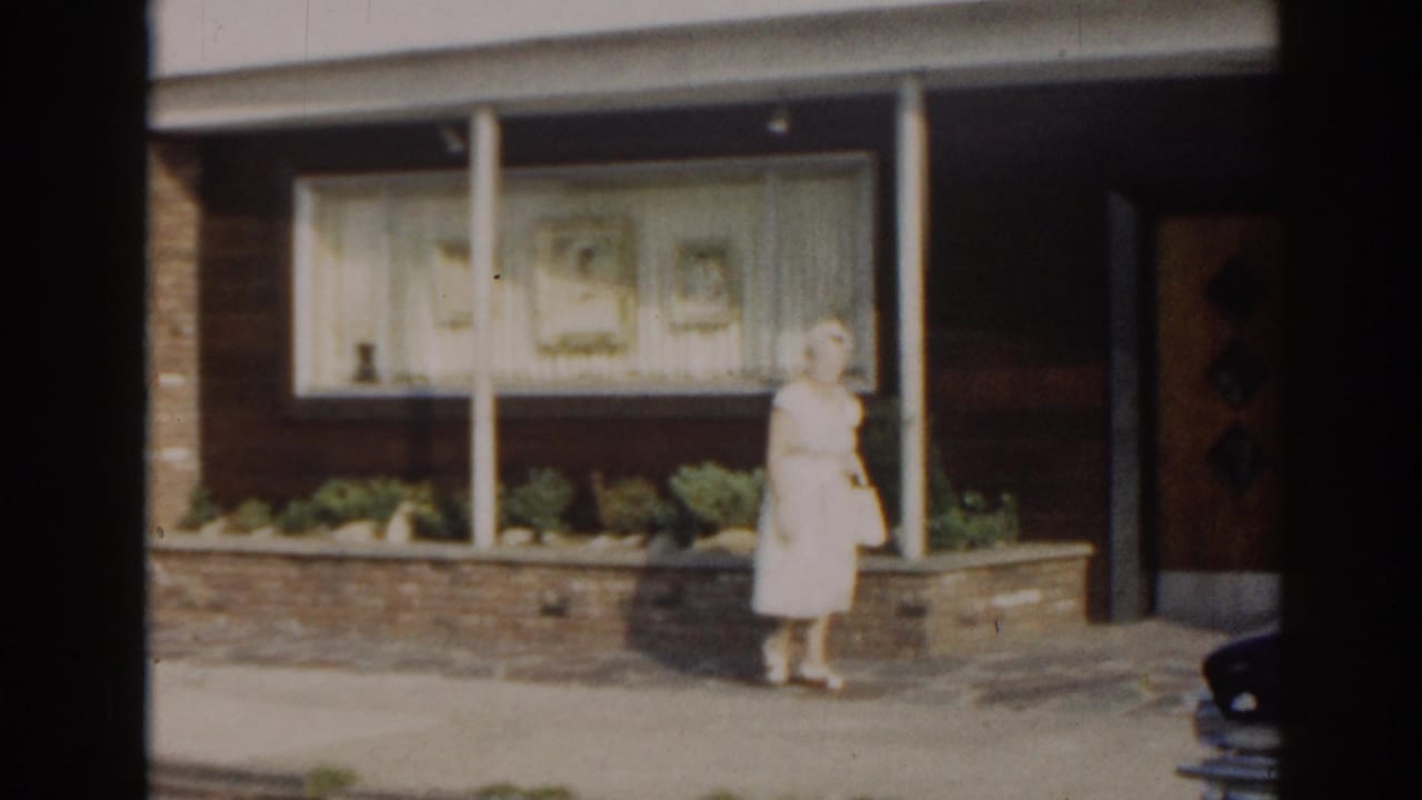 Woman in a light dress standing near a brick planter outside a building with large windows.