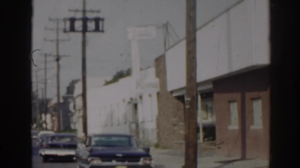 1963 New Jersey street view with parked cars, utility poles, and low buildings seen through soft 8mm exposure.