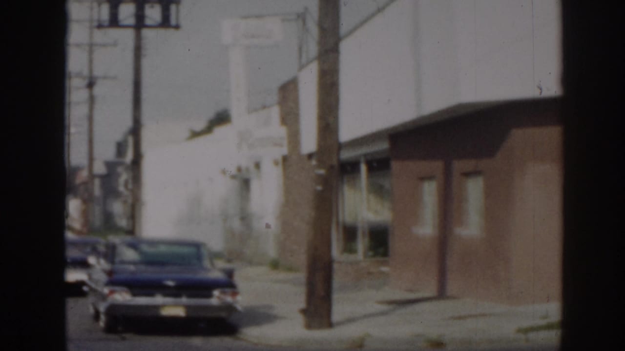Parked sedan in front of white and brown street-facing buildings.