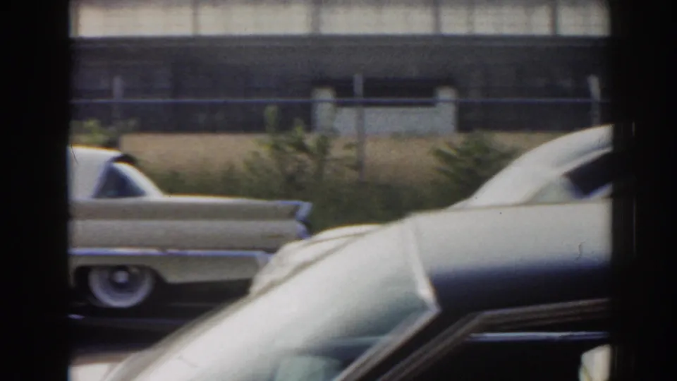 1963 New Jersey 8mm frame showing light-colored decorated cars passing the camera behind a dark window frame.