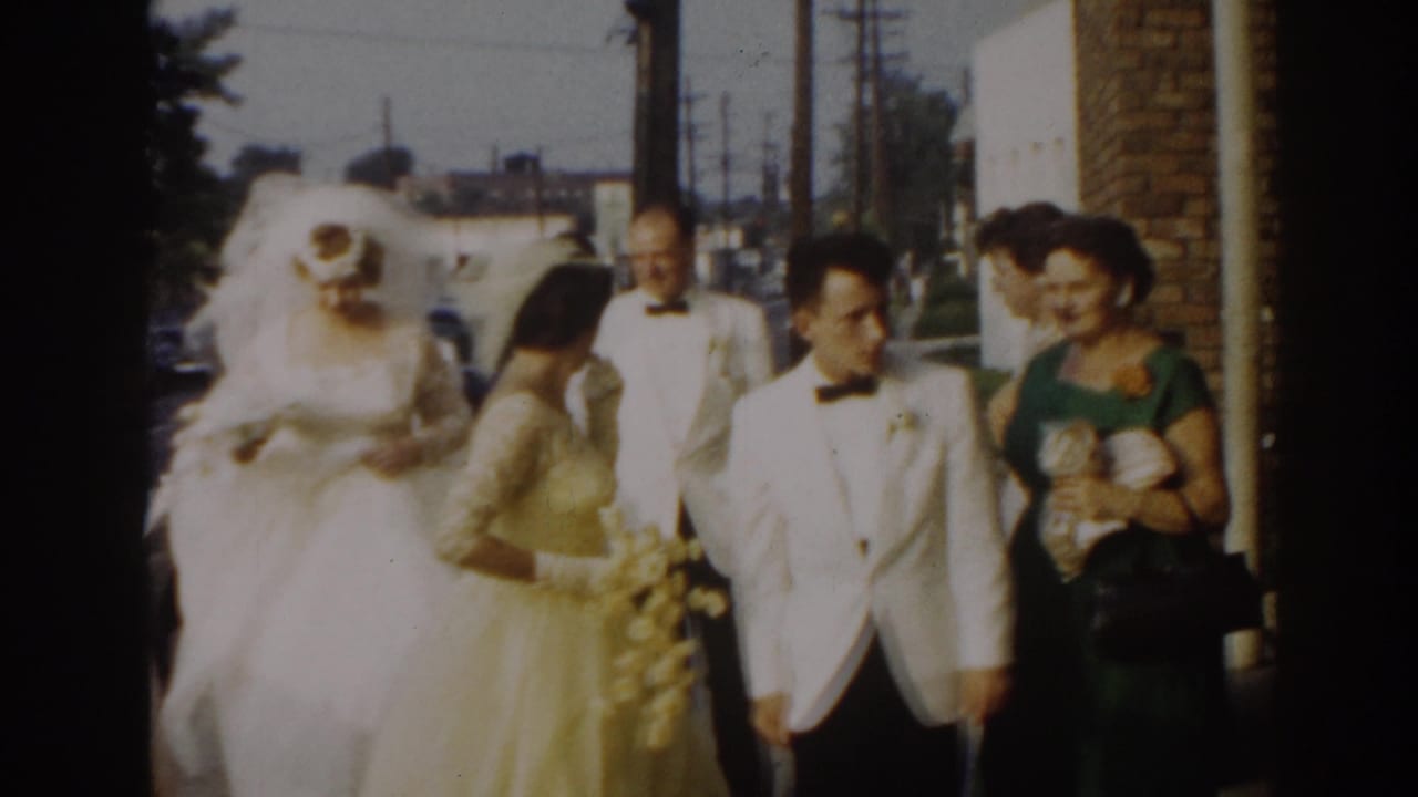 Bride and groom walk past guests while a woman in green holds a bouquet.