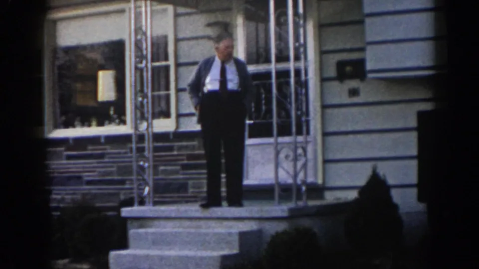 Adult man remains on the porch of a New Jersey suburban home, framed by the doorway, window, steps, and railings.