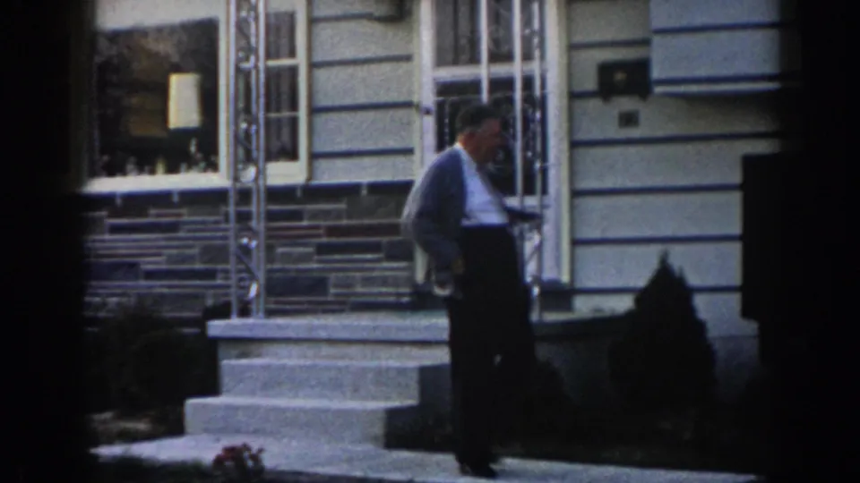 Adult man moves off the front steps of a New Jersey home, with metal porch railings and shrubs visible behind him.