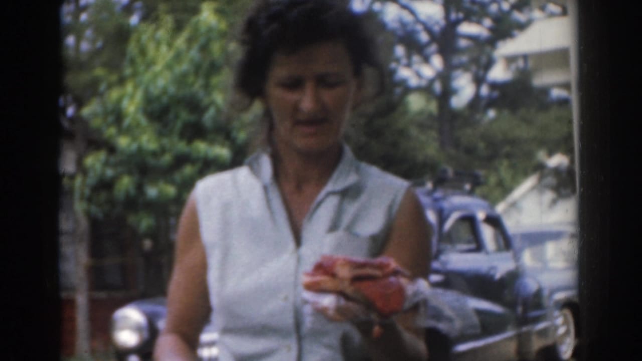 Woman looks down while holding a wrapped sandwich, with trees and a parked car in the background.