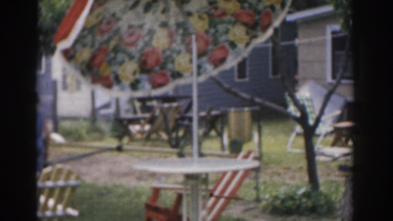 Floral patio umbrella, picnic table, lawn chairs, and house exterior in a backyard.