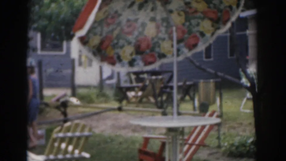 1963 New Jersey backyard frame with a partial child or small figure at left, lawn chairs, floral umbrella, and house exterior.