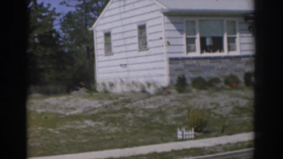 1963 New Jersey 8mm frame showing a white house with porch windows, stone foundation, shrubs, sidewalk, and tiny fence.