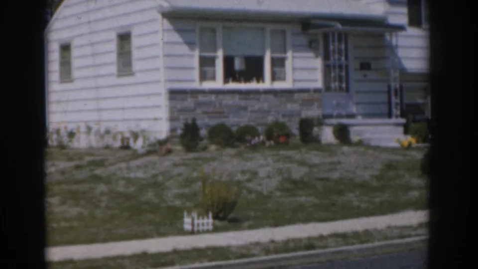 1963 New Jersey 8mm frame with a closer view of the house front, entry steps, picture window, stone wall, shrubs, and sidewalk.