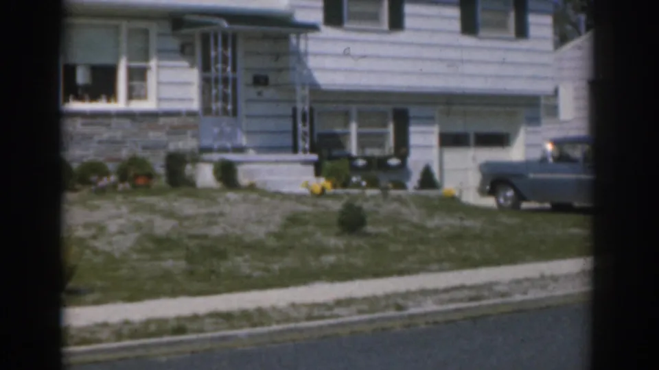 1963 New Jersey home-movie frame showing a blue station wagon partly in the driveway beside a white suburban house.