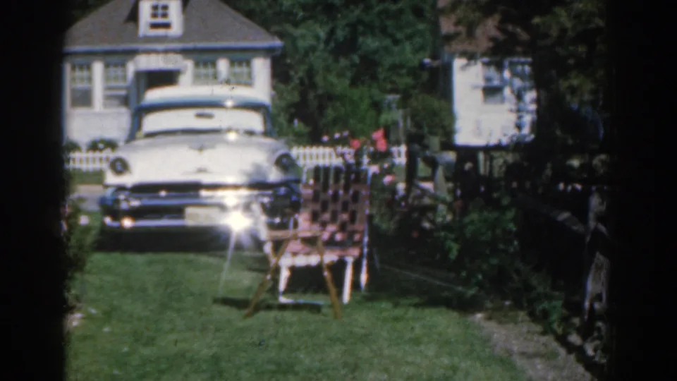 The home-movie view holds on a white car, garden chair, roses, and suburban house exterior in New Jersey.