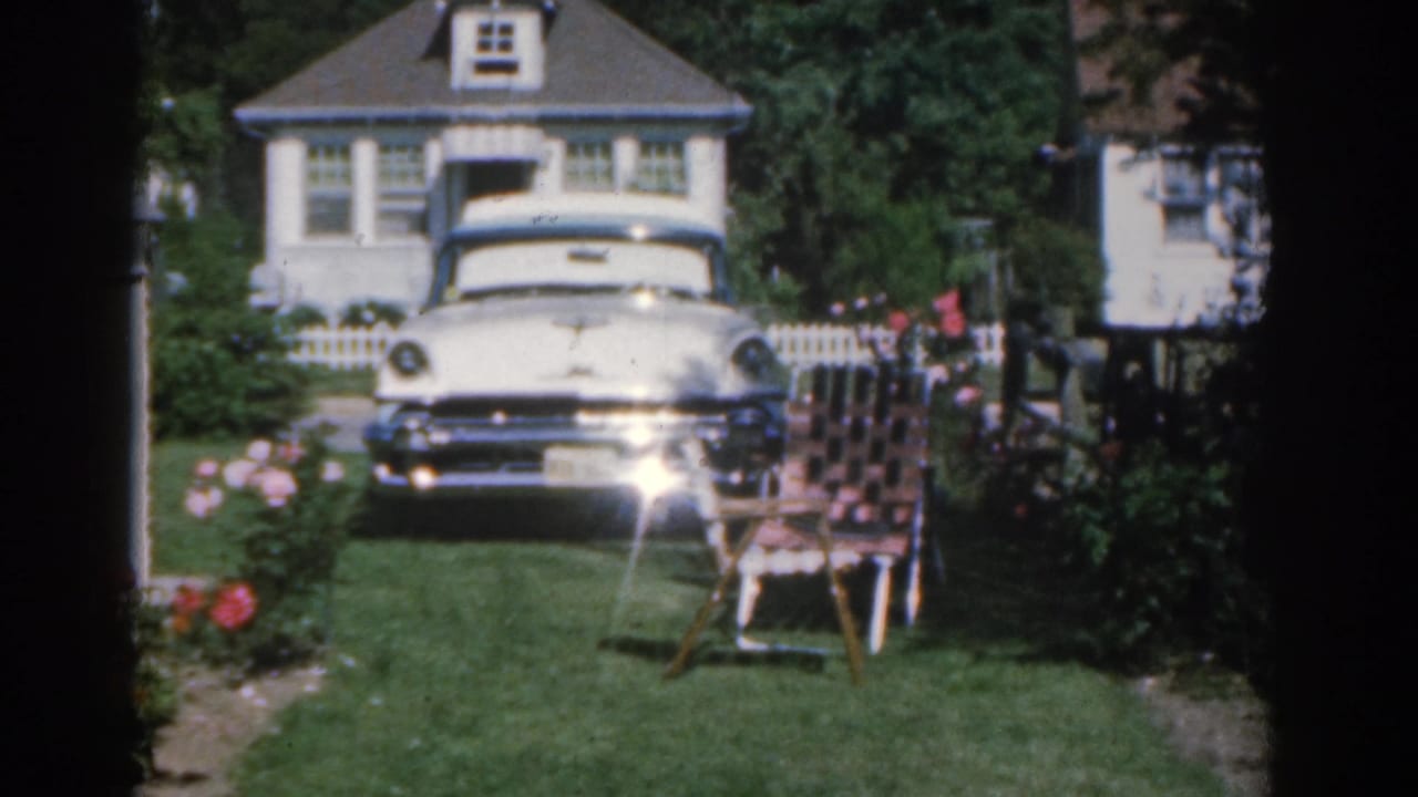 White sedan, front lawn, rose bushes, and house seen from a slightly shifted angle.