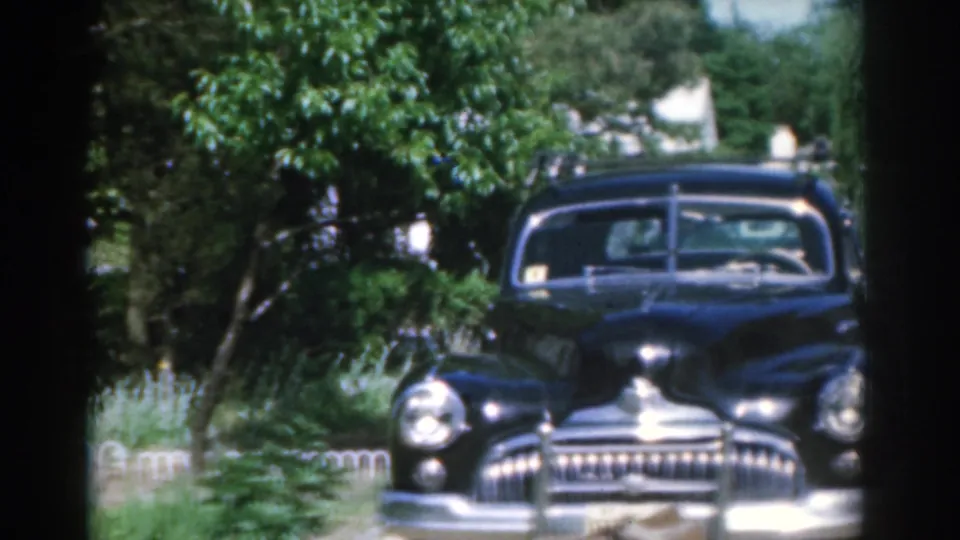 The final frame centers the black classic car's chrome grille and windshield in a leafy New Jersey residential setting.