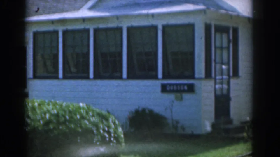 1963 New Jersey 8mm frame showing a white suburban house with dark shutters, front window, lawn, hedges, and a readable Dobson sign.
