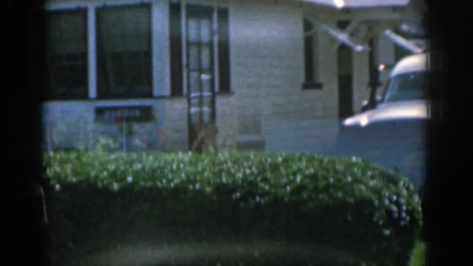 1963 New Jersey 8mm frame with a closer view of the house front, hedges, readable Dobson sign, doorway, and part of a parked car.