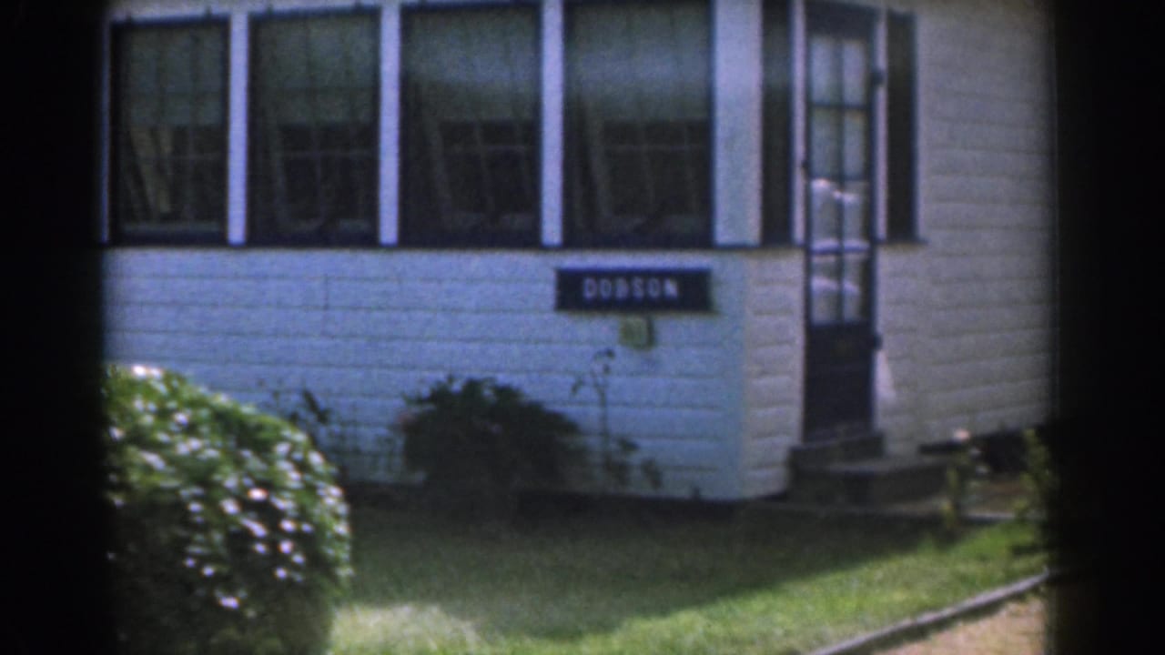 White house exterior with black shutters, a DOBSON sign, lawn, shrubs, and front steps.