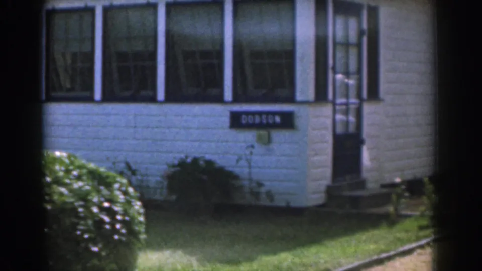 1963 New Jersey 8mm frame showing a white house with black trim, a DOBSON sign, front windows, lawn, and shrubs.