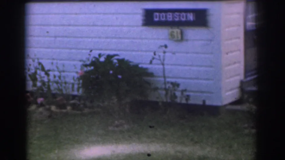 Close view of a DOBSON house sign, number area, white siding, and low garden plants in a New Jersey suburban exterior.