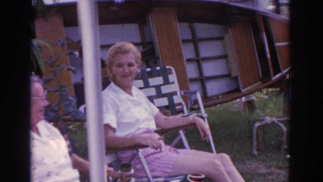 Two women sit outdoors near porch posts and lawn chairs.
