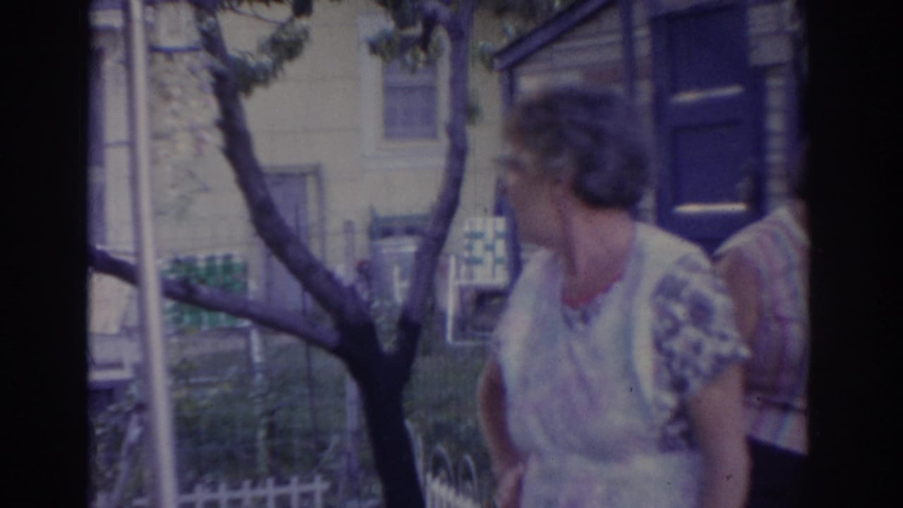 Woman turns beside a blue door with a tree and house behind her.