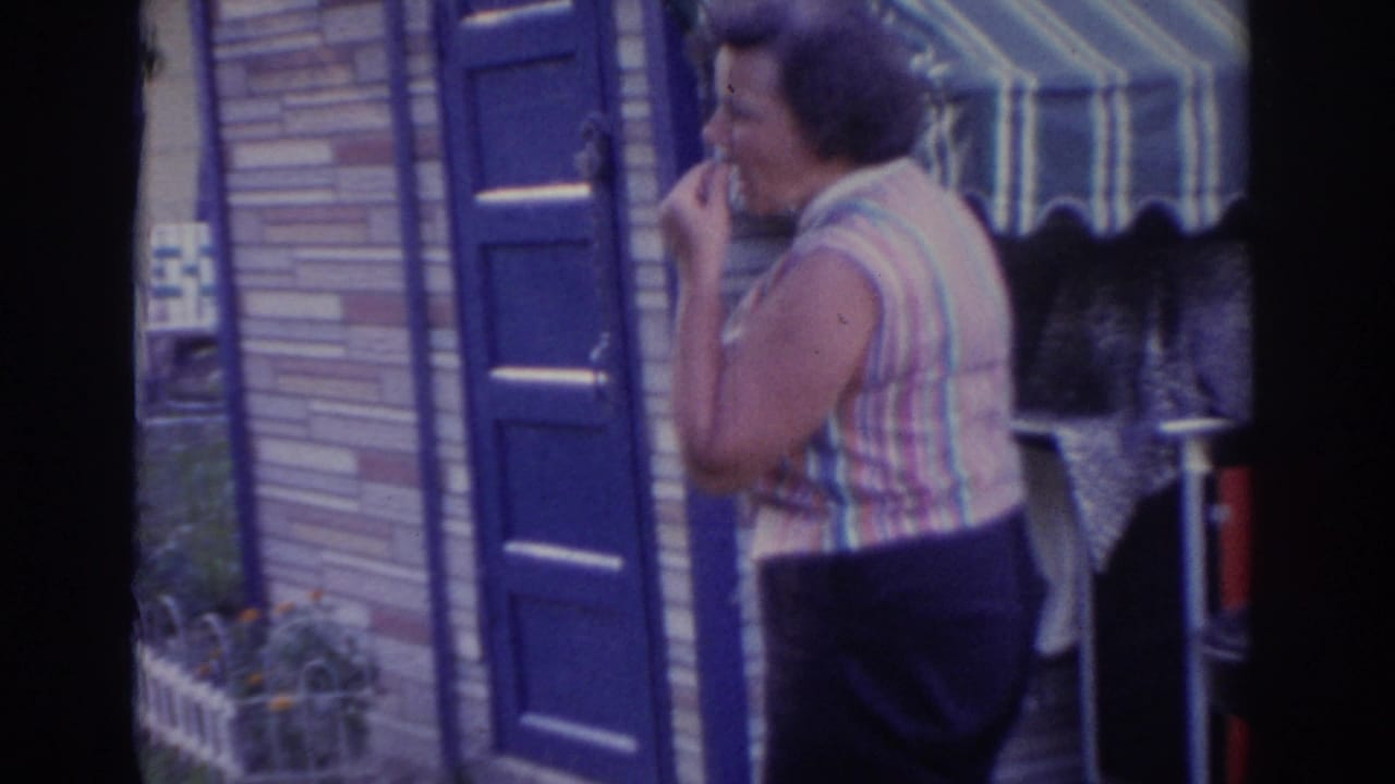 Woman in a striped sleeveless top stands by a blue door and awning, tasting food.