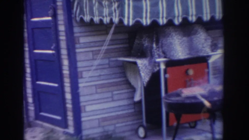 1963 New Jersey frame showing the outdoor cooking setup with a small red grill, chair, striped awning, brick wall, and blue door.