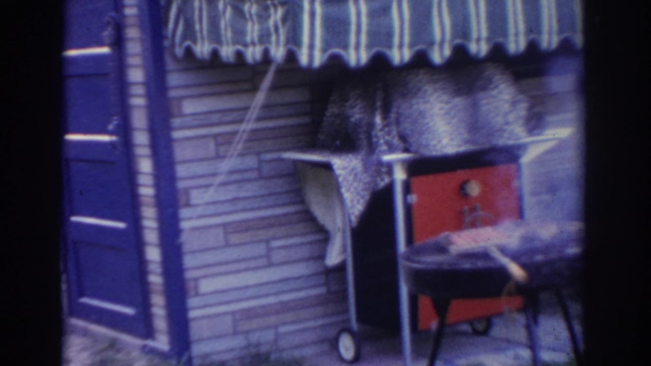 Smoking outdoor grill beneath a striped awning beside a red cooler and brick wall.