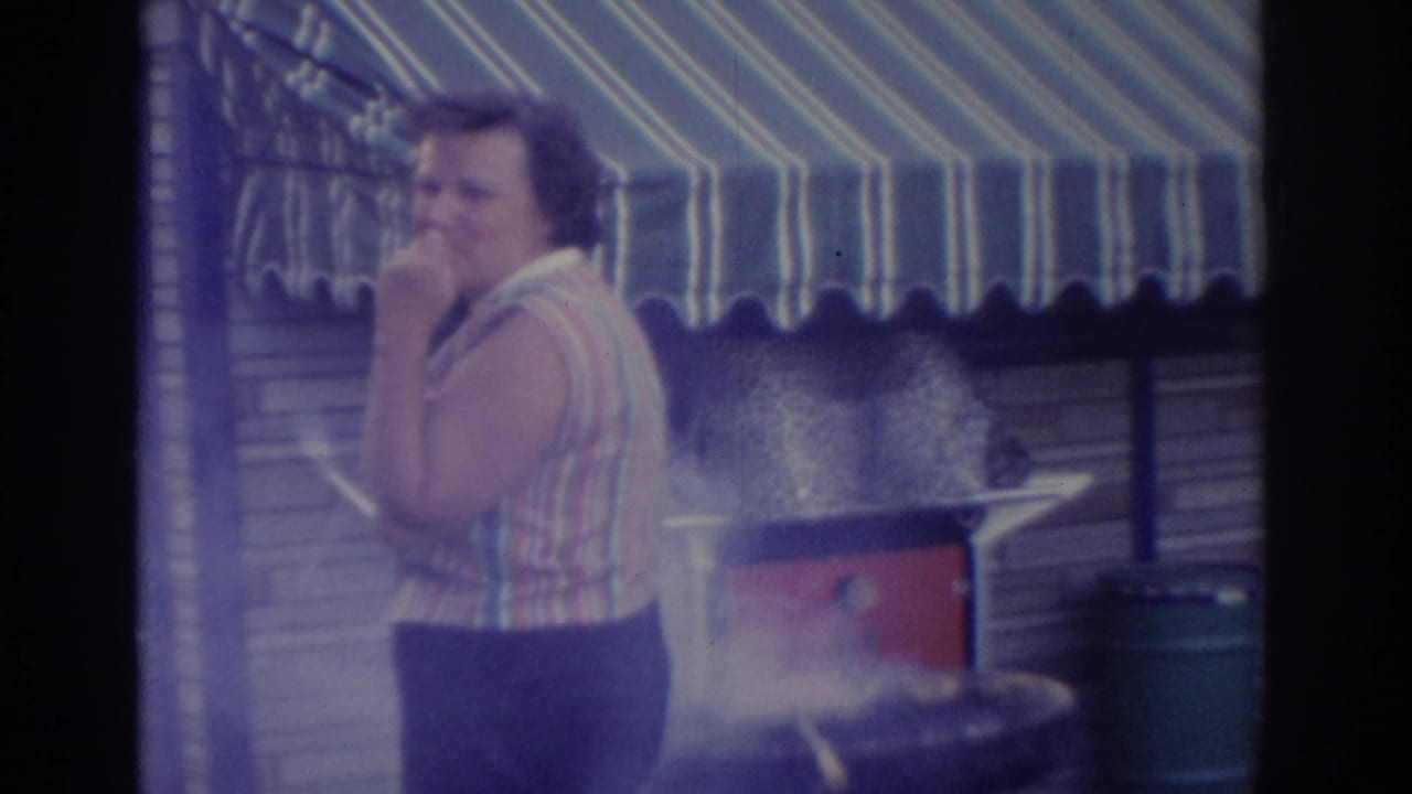 Woman faces the camera while touching her face beside a smoking grill and striped awning.