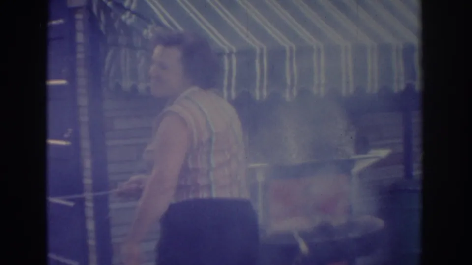 The woman appears in profile beside the smoking barbecue grill, with the striped awning and patio area behind her.