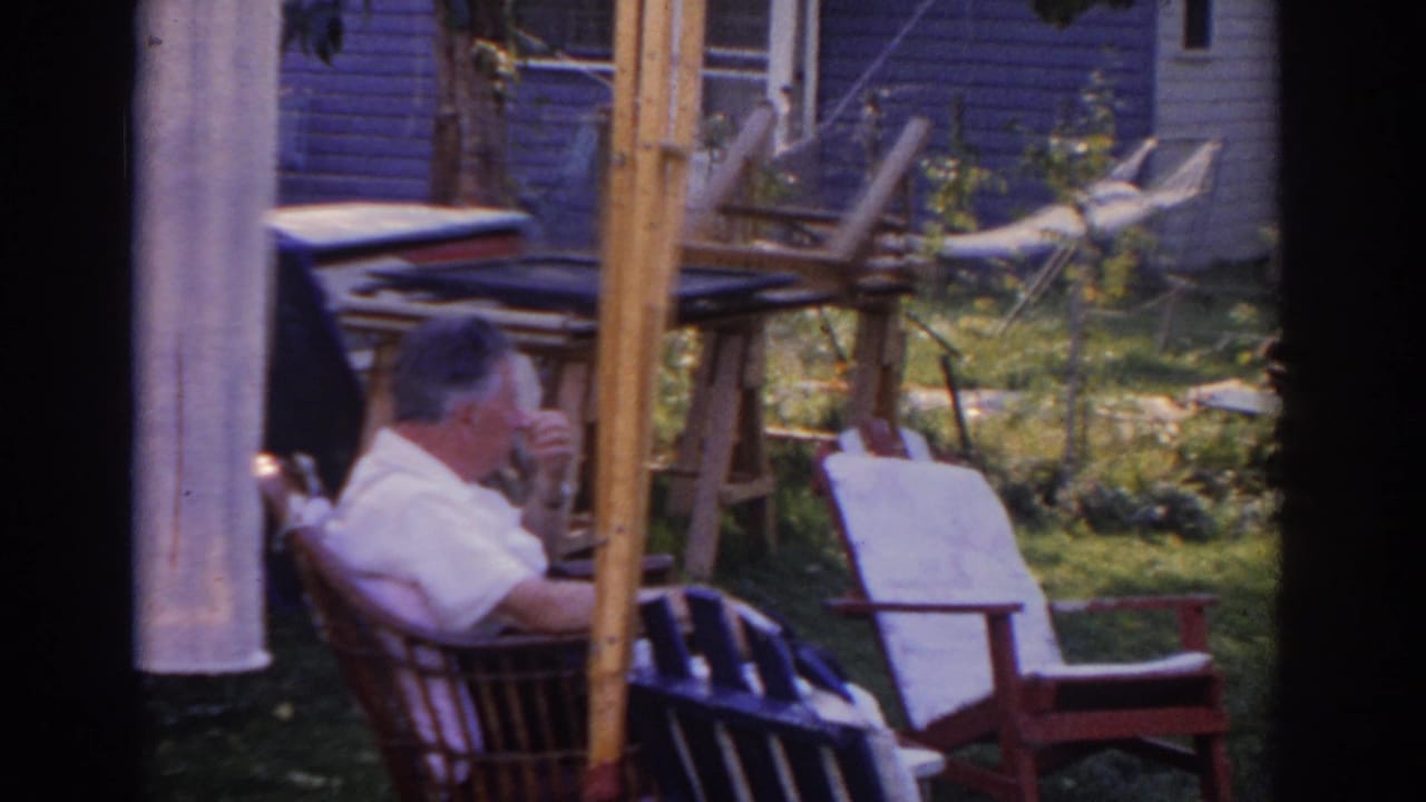 In 1963 New Jersey home-movie footage, a man sits in a wicker rocker near lawn furniture and a purple-sided house.