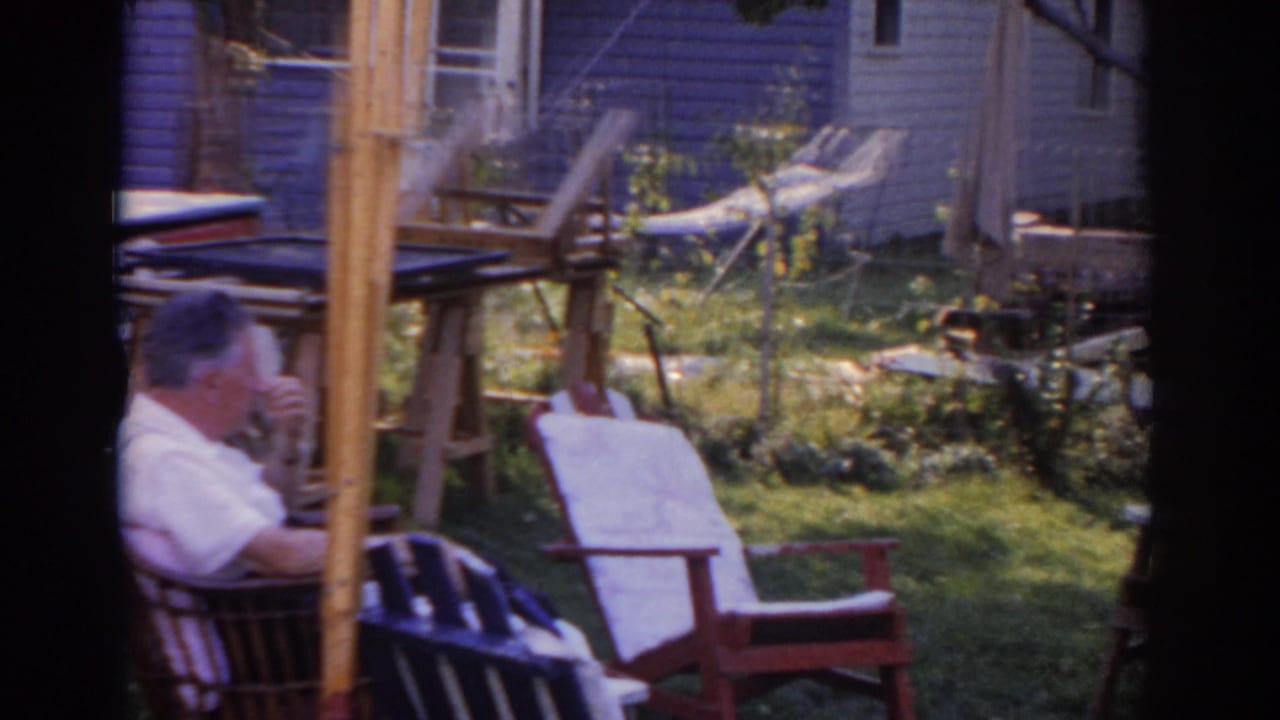 Man sits in a backyard chair with lawn furniture and a house behind him.