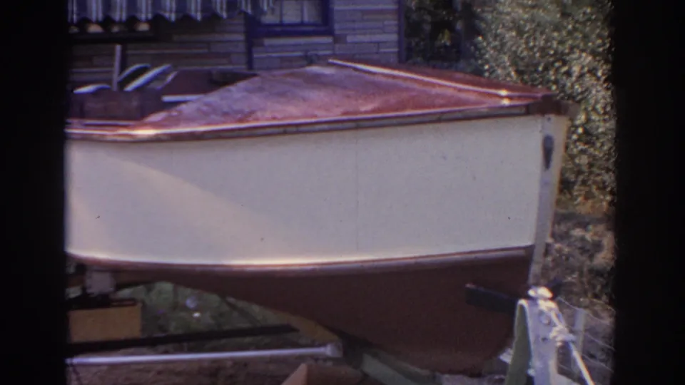 A small cream-and-red boat on a trailer fills the lower frame, with a striped awning and house exterior behind it.